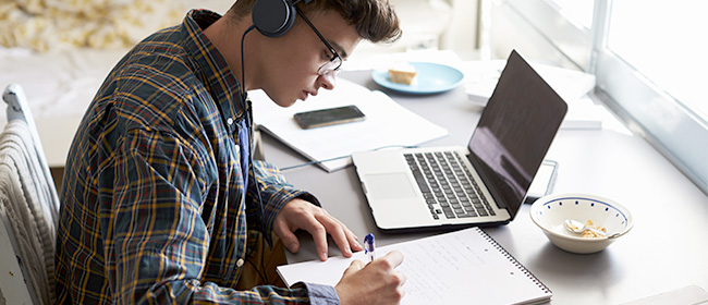 Two students participating in a live O Level online class on a large monitor with textbooks and a laptop on their desk